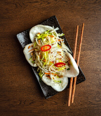 Asian cuisine. Salad of Asian noodles and cabbage with rice chips on a black plate.