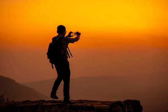 Man hold smartphone on the cliff of the mountain on sunset background