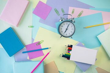 Back to school, stationery, alarm clock, stack of books, paper and colored pencils on student's desk, top view