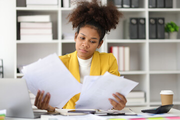 Stress and pressure of overwork. African woman in office stressed with paperwork and worried about...