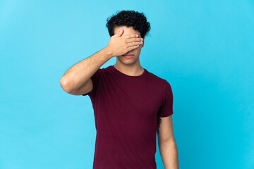 Young Venezuelan man isolated on blue background covering eyes by hands. Do not want to see...