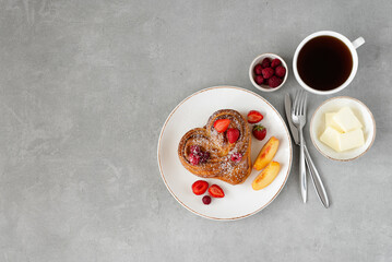 Valentine's day breakfast on gray background. Bun with butter and berries on a white plate and a cup of coffee