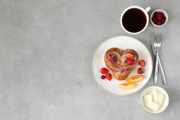 Obraz na płótnie Canvas Valentine's day breakfast on gray background. Bun with butter and berries on a white plate and a cup of coffee