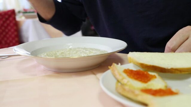 Hands of man eating porridge in canteen with red chairs