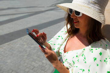 Beautiful tourist girl with hat holding mobile phone and talking at the city square.