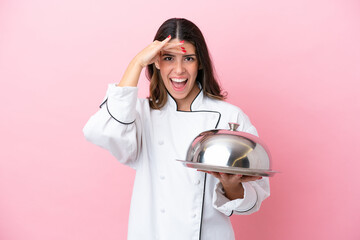 Young Italian chef woman holding tray with lid isolated on pink background doing surprise gesture...