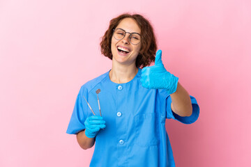 Woman English dentist holding tools over isolated on pink background with thumbs up because something good has happened