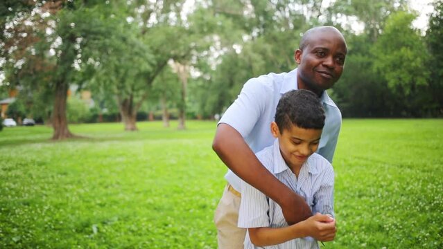 The father hugs and tickles his son in the park on a summer day