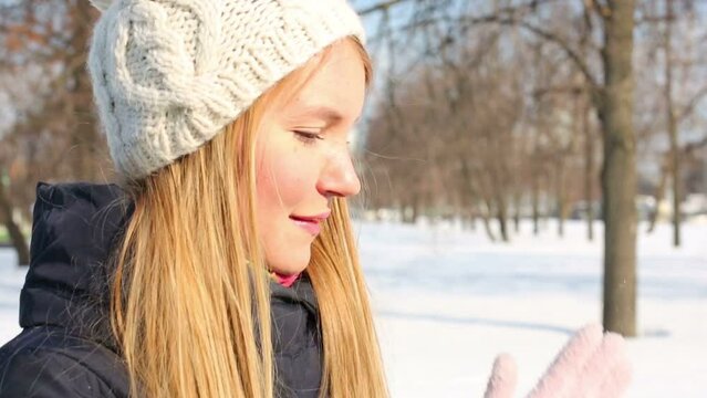 Young woman in hat shakes off the snow from gloves in park