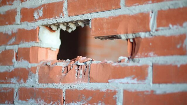 Hands on man holding perforator and making hole in brick wall