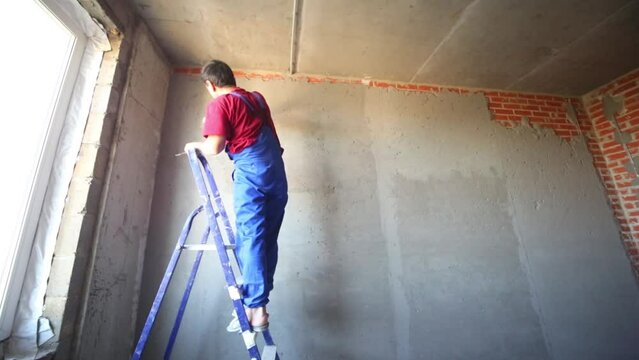 Working man stands on ladder and makes plaster on wall