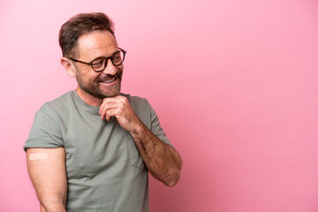 Middle age man wearing a band aids isolated on pink background thinking an idea and looking side - obrazy, fototapety, plakaty