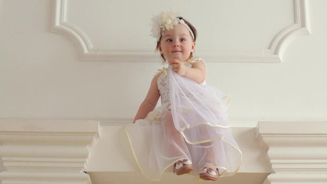Beautiful baby girl in costume of bride sits on fireplace 