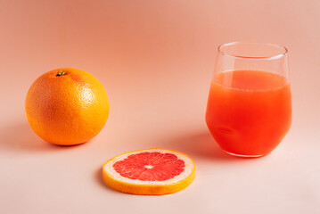 Grapefruit next to a slice and a glass with its orange-red juice on a pink background,close-up.