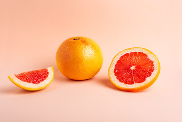 Grapefruit next to a slice and a piece on a pink background,close-up.