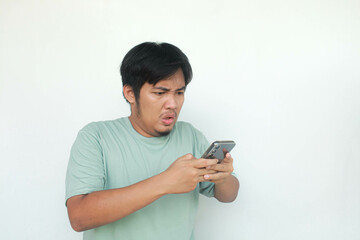 Young Asian man showing rage expression while typing on his mobile phone. Isolated in gray background.