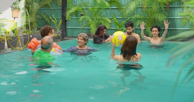 Happy Indian elder older group family adult couple mom dad play ball water pool teen girl young boy child enjoy fun joy day trip outdoor home old aged man male female kid holiday hotel resort park