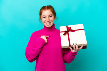 Young caucasian reddish woman holding a gift isolated on blue background with surprise facial expression