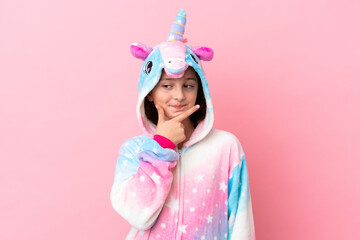Little caucasian woman wearing a unicorn pajama isolated on pink background thinking
