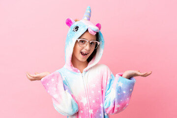 Little caucasian woman wearing a unicorn pajama isolated on pink background