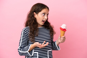 Little caucasian girl holding an ice cream isolated on pink background with surprise expression while looking side