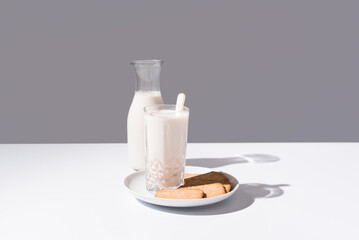 Vaso de leche y botella llena de leche. Desayuno con galletas en un plato sobre fondo gris