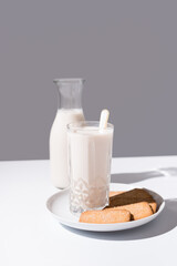 Vaso de leche y botella llena de leche. Desayuno con galletas en un plato sobre fondo gris