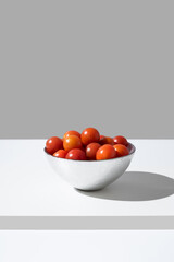 Tomates cherry maduros en un bol plateado sobre fondo gris