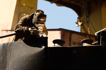 Skilled welder in protective gear at work, joining metal pieces on industrial equipment. Sparks fly...