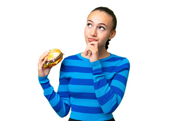 Young Arab woman holding a burger over isolated background and looking up