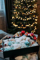 A box with Christmas toys wrapped in paper for storage. In the background there is an artificial Christmas tree with a garland with yellow lights, but without toys. Decorate the Christmas tree
