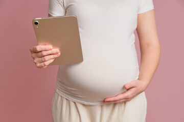Pregnant woman holding digital tablet, studio pink background. Pregnancy and modern technology concept