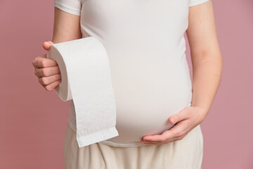 Pregnant woman holding toilet paper, studio pink background. Concept of pregnancy and stomach...