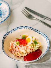 Mayonnaise salad with crab meat, decorated with beetroot mousse in restaurant-style plating. Imitation crab salad with crab sticks or meat and eggs in bowl on marble background. Vertical, copyspace