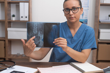 Woman traumatologist points finger at X-ray picture talking to patient online looking at camera...