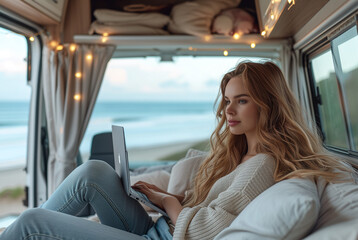 A beautiful woman in stylish clothes works with a laptop in a trailer, mobile home on the ocean. Freelancer. Work remotely. trailer home. Camping vacation