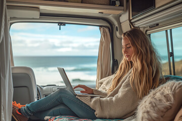 Fototapeta na wymiar A beautiful woman in stylish clothes works with a laptop in a trailer, mobile home on the ocean. Freelancer. Work remotely. trailer home. Camping vacation