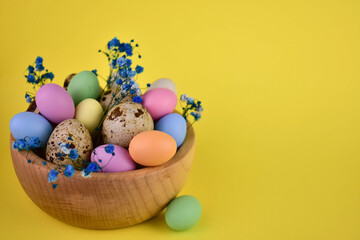 Multi-colored Easter eggs in a wooden bowl on a yellow background.Copy space.
