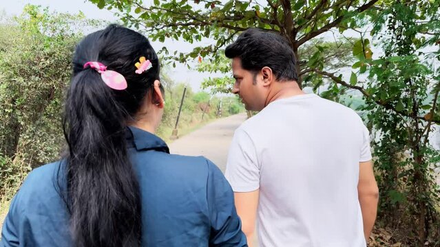 Rear view of a couple walking on a secluded road surrounded by nature depicting a peaceful stroll or conversation
