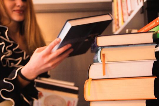 A red-haired girl with graceful fingers in a black ruffled blouse selects books to read in the library and puts them in a stack of books. Day of Knowledge