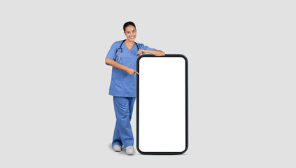 A friendly female doctor in blue scrubs leans on a giant smartphone