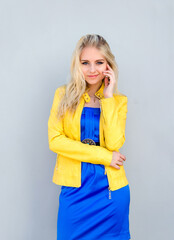 beautiful blonde woman in a yellow jacket and blue dress posing in the studio.