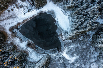 Aerial view of a lake in winter with ice, snow and nearby road close to a mountain