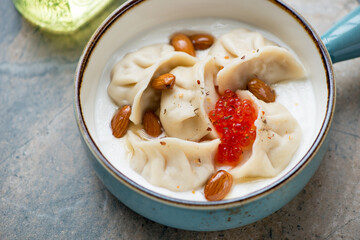 Vareniki dumplings served with yogurt and red caviar in a turquoise bowl, middle close-up,...