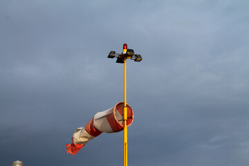 Windsock torn by the wind. Mast with red signal lights of the aerodrome against a dramatic stormy sky. Aerodrome aviation equipment at sunset against a dramatic stormy sky.