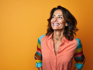 Middle aged hispanic woman smiling happily in front of a colorful orange background. 
