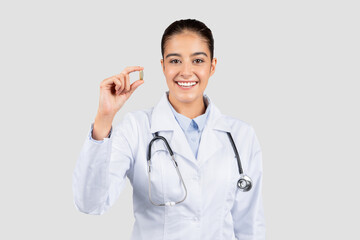 Happy european doctor in a white lab coat holding up a single capsule