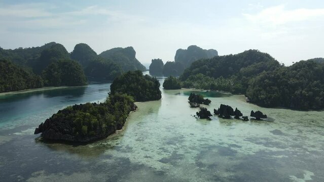 aerial shoot, flight over colourful lagoon with Turquoise water, sand beach and palm trees in Raja Ampat Indonesia