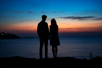 Silhouette of couple man and woman in front of twilight sunset. Dark colors sky beautiful sea sunset. Two people in romantic relationship holding their hands. Tranquil standing full body photo