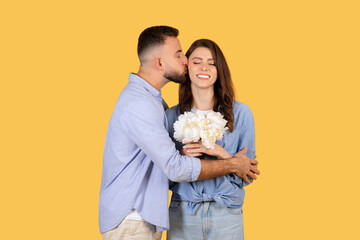 Man kissing woman on cheek, she holds flowers, expressing affection